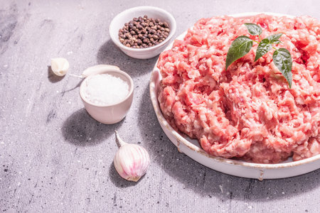 Minced meat in a ceramic stand. Raw pork, fresh herb leaves, spices, sea salt, and garlic. Modern...