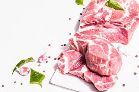 Raw pork meat, sliced cuts. Fresh meat, dry sumac, garlic and basil leaves. Healthy cooking food concept, trendy hard light, dark shadow. White putty background, copy spaceの写真素材