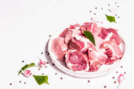 Diced raw pork meat with dry sumac, fresh garlic, and basil leaves. Healthy cooking food concept, trendy hard light, dark shadow. White putty background, copy spaceの写真素材