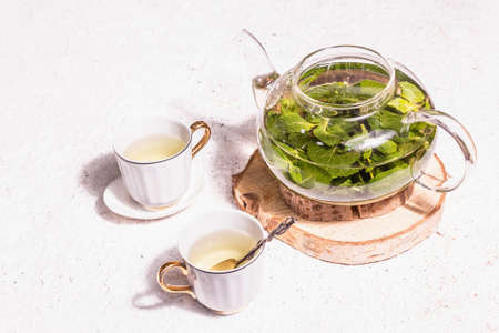 Teatime concept. Aromatic mint tea, ceramic cups on stands. Modern hard light, dark shadow. Plaster background, copy spaceの写真素材