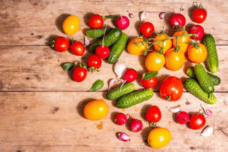 Food, harvesting, summer concept. Assortment of ripe organic farmer red and yellow tomatoes, cucumbers, radish, garlic, and fresh basil leaves. Old wooden table, top viewの写真素材
