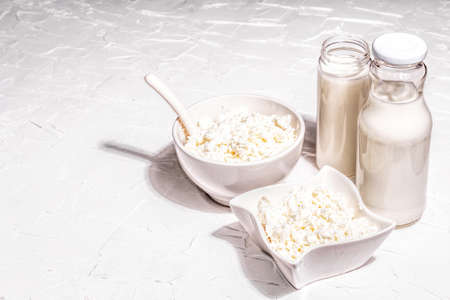 Cottage cheese in a ceramic bowl with milk in bottles. Homemade dairy product on a deep plate. White putty background, copy spaceの写真素材
