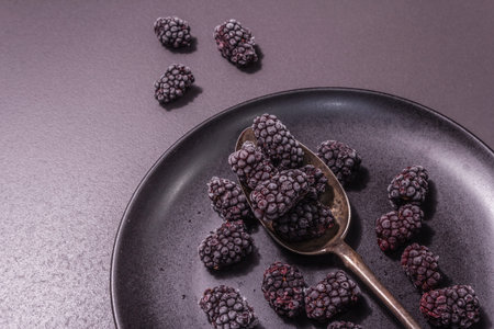 Blackberries on a ceramic plate. Frozen fruits for a healthy food diet. Minimalistic concept, black...