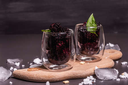 Refreshing blackberry fruit drink. Cold summer berry cocktail, modern hard light, dark shadow. Black stone concrete background, copy spaceの写真素材