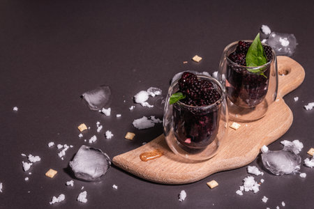 Refreshing blackberry fruit drink. Cold summer berry cocktail, modern hard light, dark shadow. Black stone concrete background, copy spaceの写真素材