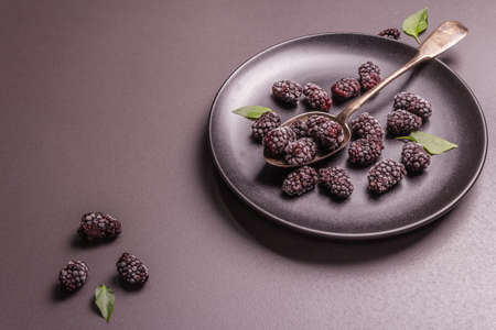 Blackberries on a ceramic plate. Frozen fruits for a healthy food diet. Minimalistic concept, black stone concrete background, hard light, dark shadow, flat layの写真素材