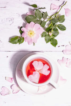 Tea from rose hips flowers. Summer vitamin drink, hard light, dark shadow. White wooden background, top viewの写真素材