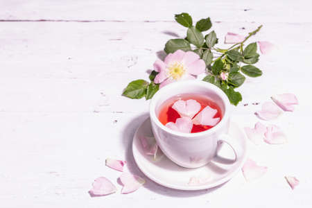 Tea from rose hips flowers. Summer vitamin drink, hard light, dark shadow. White wooden background, copy spaceの写真素材