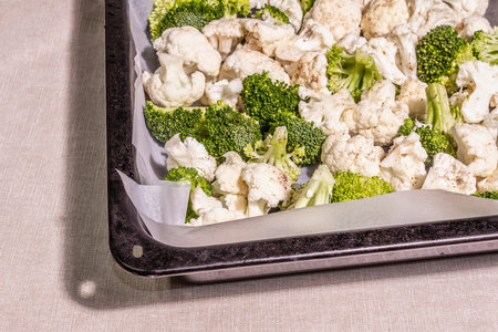 Assorted cauliflower and broccoli, ready to bake. The cooking food concept for a healthy lifestyle. A hard light, dark shadow, baking tray on a table, copy spaceの写真素材