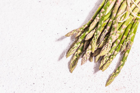 Ripe asparagus on a white textured plaster background. Fresh green ingredients ready for cooking healthy food. A modern hard light, dark shadow, top viewの写真素材
