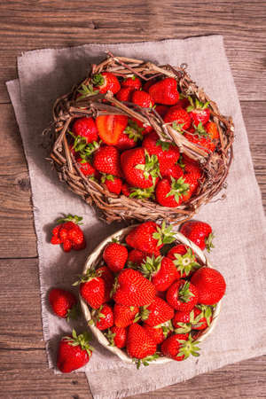Fresh ripe strawberry in a wicker basket. Sweet summer fruit, healthy food. Modern hard light, dark shadow. Vintage wooden boards background, top viewの写真素材