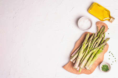 Ripe asparagus on a wooden chopping board. Fresh ingredients ready for cooking healthy food. Modern hard light, dark shadow. White putty background, top viewの写真素材
