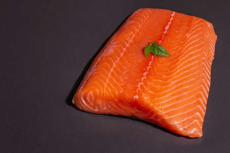 Fresh raw salmon or trout sea fish fillet on black stone background. Useful ingredient for healthy food, source of Omega 3. A modern hard light, dark shadow, culinary wallpaper, copy spaceの写真素材