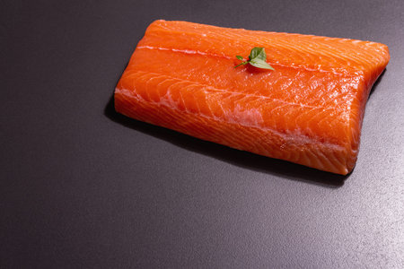 Fresh raw salmon or trout sea fish fillet on black stone background. Useful ingredient for healthy...