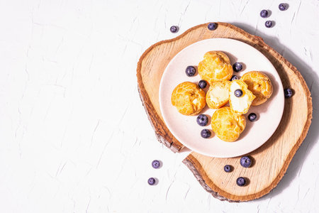 Profiteroles with blueberries. Custard cakes, Eclair, cream puff on a wooden stand, fashionable hard...