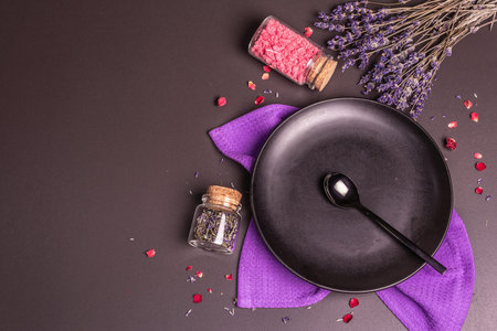 Table setting for a sweet dessert. Plate, spoon, lavender flowers, rose petals, and sweet pink sugar. Black stone concrete background, top viewの写真素材