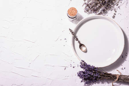 Table setting for a sweet dessert. Plate, vintage silver spoon, lavender flowers. Modern hard light, dark shadow. White putty background, top viewの写真素材