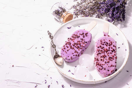 Purple Lavender flavored ice cream. Flower bouquet, vintage silver spoon, ceramic stand. Modern hard light, dark shadow. White putty background, copy spaceの写真素材