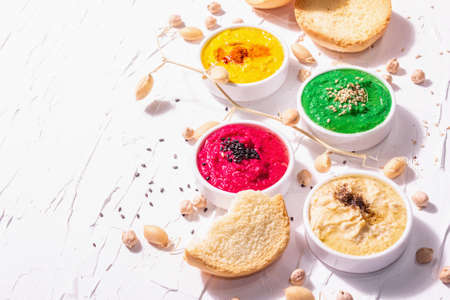 Various hummus dips, the flat lay of hummus in different colors with spinach, beetroot, turmeric and vegetables, vegan snack. White putty background, copy spaceの写真素材