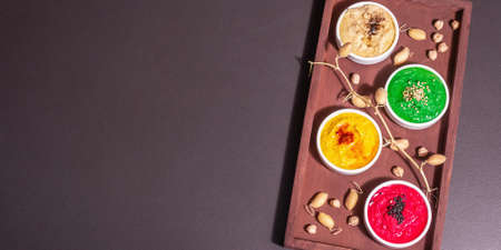 Colorful hummus bowls, healthy vegan dips. Traditional Middle Eastern food. Beets, spinach, aromatic spices. Black stone concrete background, top view, bannerの写真素材