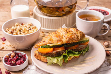 Healthy breakfast concept. Morning good mood with tea, croissant, granola, milk, and jam. Vintage wooden table, close upの写真素材