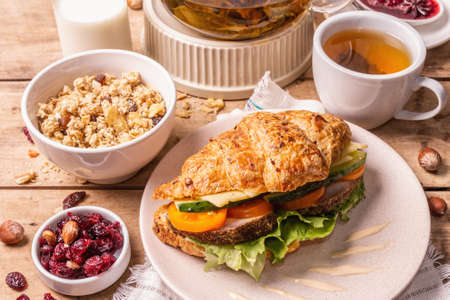Healthy breakfast concept. Morning good mood with tea, croissant, granola, milk, and jam. Vintage wooden table, close upの写真素材