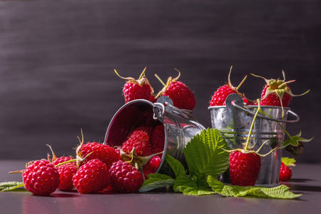 Ripe raspberries on a black stone concrete background. Small buckets, fresh leaves, new harvest....