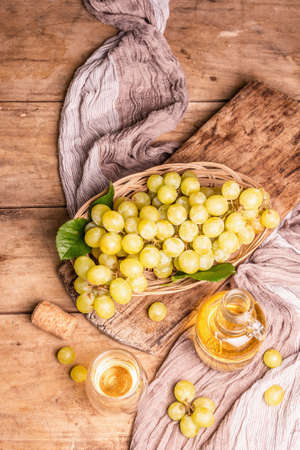 White wine and grape in a wicker basket. Fresh fruits, glass, and bottle. Old wooden boards background, top viewの写真素材