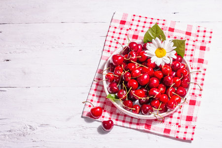 Fresh ripe sweet cherries in a bowl with droplets of water. Old white wooden table, top view