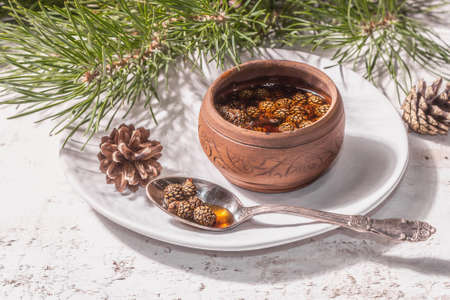 Sweet pine cone jam. Traditional Siberian dessert, fresh evergreen branches. Trendy hard light, dark shadow. White wooden background, close upの写真素材