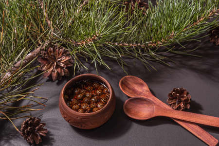 Sweet pine cone jam. Traditional Siberian dessert, fresh evergreen branches. Trendy hard light, dark shadow. Black stone concrete background, flat layの写真素材