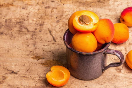 Ripe apricots in a vintage iron mug. Sweet fruits, old wooden table, copy spaceの写真素材
