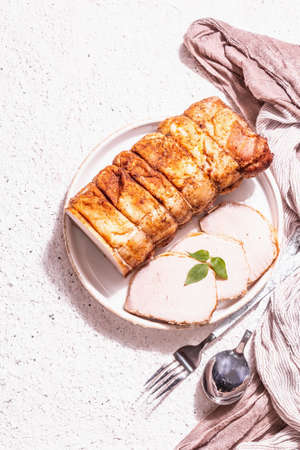 Baked pork loin on a ceramic stand with cutlery. A trendy hard light, dark shadow, white putty background, top viewの写真素材