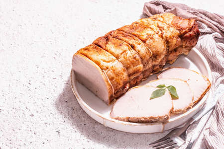 Baked pork loin on a ceramic stand with cutlery. A trendy hard light, dark shadow, white putty background, place for textの写真素材