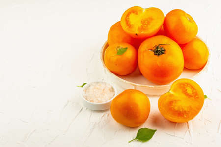 Ripe orange tomatoes with fresh basil. New harvest vegetables on a ceramic stand. White putty background, copy spaceの写真素材