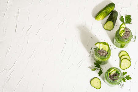 Green smoothie with cucumber in a glass jar. Fresh ripe vegetables, greens, and chia seeds. Trendy hard light, dark shadow. White putty background, top viewの写真素材