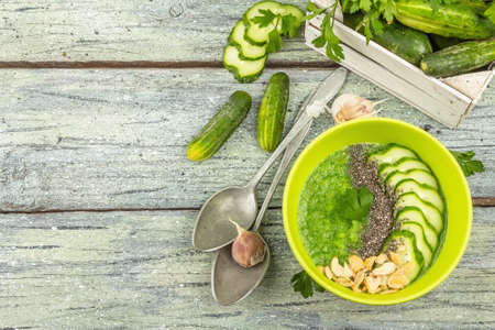 Cucumber Gazpacho. Green fresh cold summer soup. Fresh vegetables, greens, spices and cutlery. Old wooden boards background, top viewの写真素材
