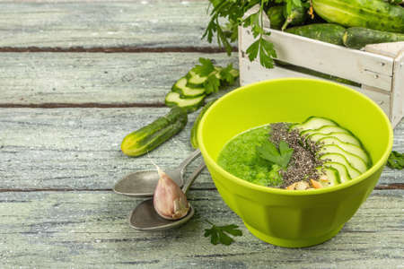 Cucumber Gazpacho. Green fresh cold summer soup. Fresh vegetables, greens, spices and cutlery. Old wooden boards background, copy spaceの写真素材