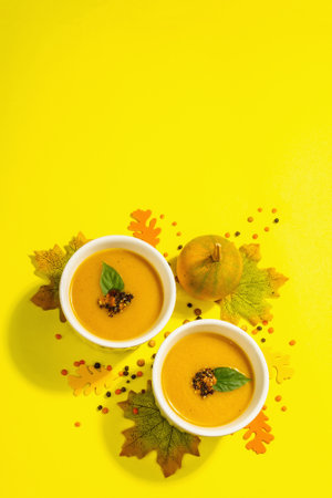Vegetable cream soup. Traditional autumn composition. Healthy hot food, spices, foliage. A trendy hard light, dark shadow, on a bright yellow background, top viewの写真素材