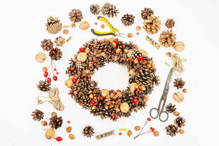 Autumn wreath of cones, nuts, and berries. Assortment from natural materials for creative composition. Handmade home decoration festive concept. White putty background, top viewの写真素材