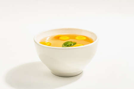 Transparent chicken broth in a ceramic bowl isolated on white background. Traditional bouillon, healthy food, ripe vegetablesの写真素材