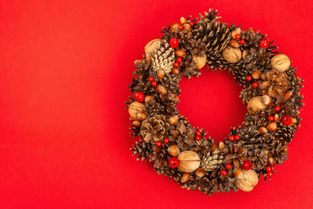 Autumn wreath of cones, nuts, and berries. Creative composition, the handmade. Home decoration festive concept. Red pastel background, top viewの写真素材