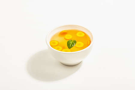 Transparent chicken broth in a ceramic bowl isolated on white background. Traditional bouillon, healthy food, ripe vegetablesの写真素材