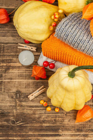 Autumn cozy composition. Ripe pumpkins, warm knitted sweaters, various berries, and candles. Thanksgiving festive greeting card. Old wooden boards background, top viewの写真素材