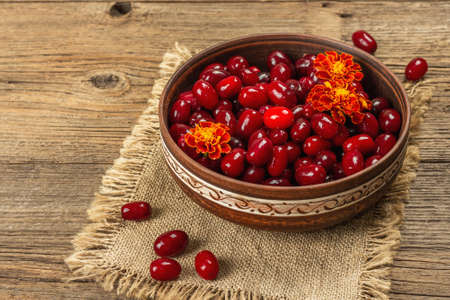 Ripe dogwood berry with bright marigold flowers. Fresh red Cornus in a ceramic bowl, old wooden table, copy spaceの写真素材