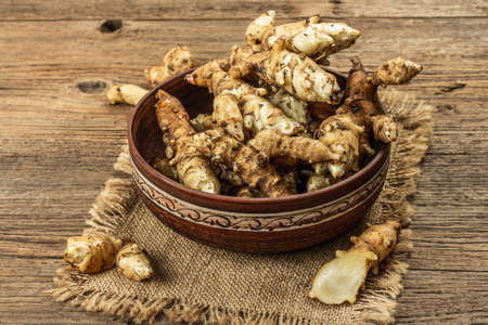 Raw Jerusalem artichoke in a bowl on wooden boards background. Freshly dug tubers ready to cook, traditional useful food, copy spaceの写真素材