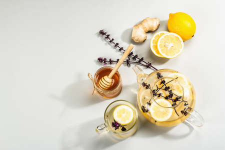 Hot ginger tea with lemon and honey in a glass cup on light gray background. Alternative medicine, natural home remedy for cold and flu, modern hard light, dark shadow, top viewの写真素材