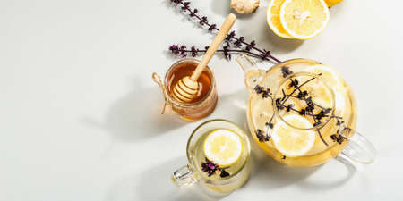 Hot ginger tea with lemon and honey in a glass cup on light gray background. Alternative medicine, natural home remedy for cold and flu, modern hard light, dark shadow, top viewの写真素材