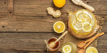 Hot ginger tea with lemon and honey in a glass cup on a wooden boards background. Alternative medicine, natural home remedy for cold and flu, banner formatの写真素材