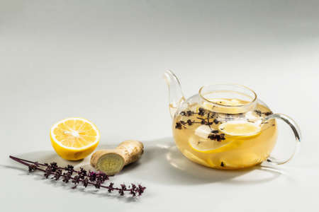 Hot ginger tea with lemon and honey in a glass cup on light gray background. Alternative medicine, natural home remedy for cold and flu, modern hard light, dark shadow, copy spaceの写真素材